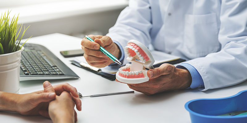 A dental professional examines a patient s teeth with a magnifying glass while seated at a desk.