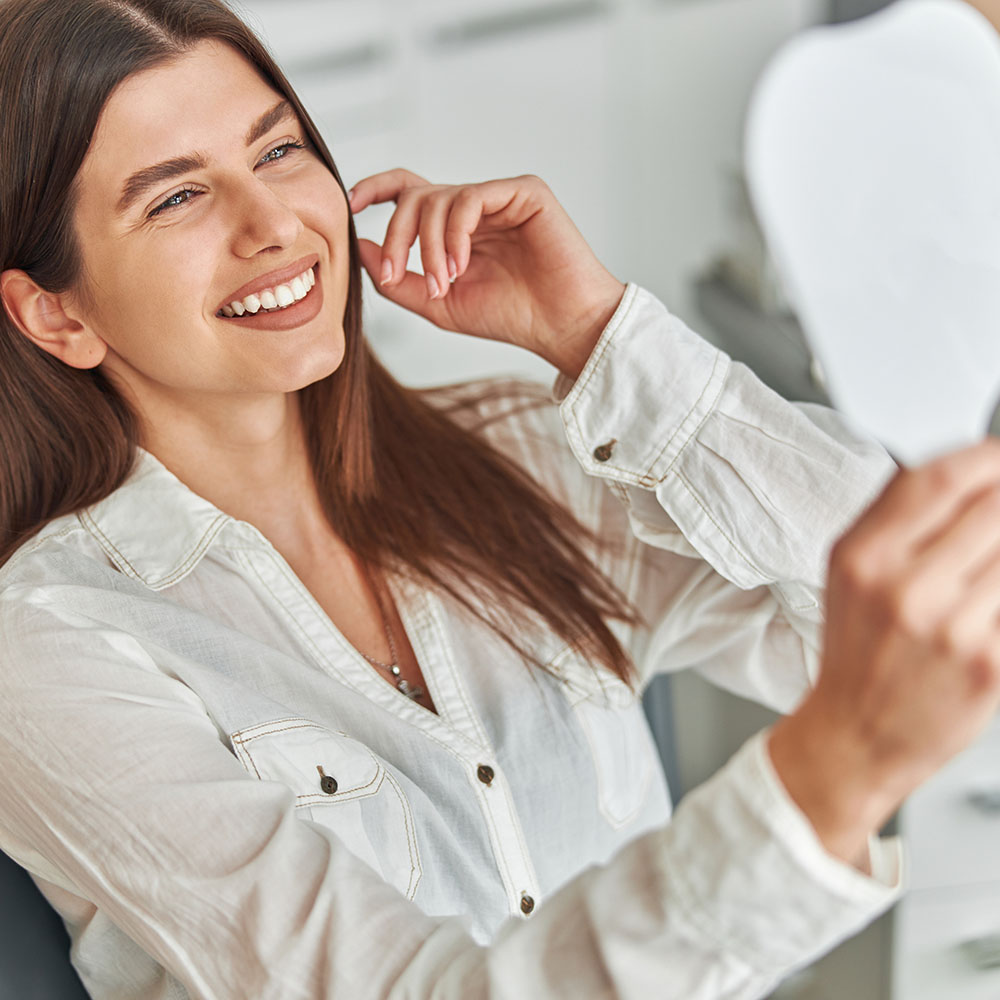 A woman smiling at her reflection in a mirror while applying makeup.